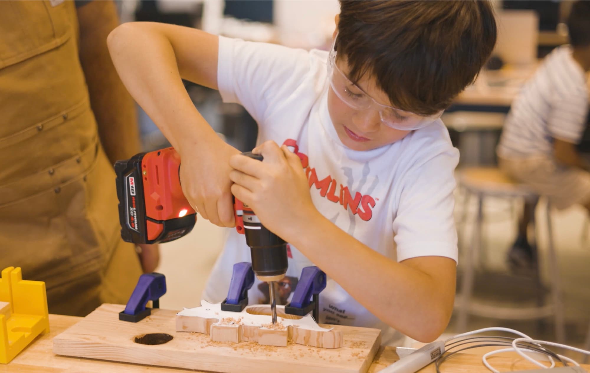 A Forge student using a power drill on a clamped wood project at the Maker rank.