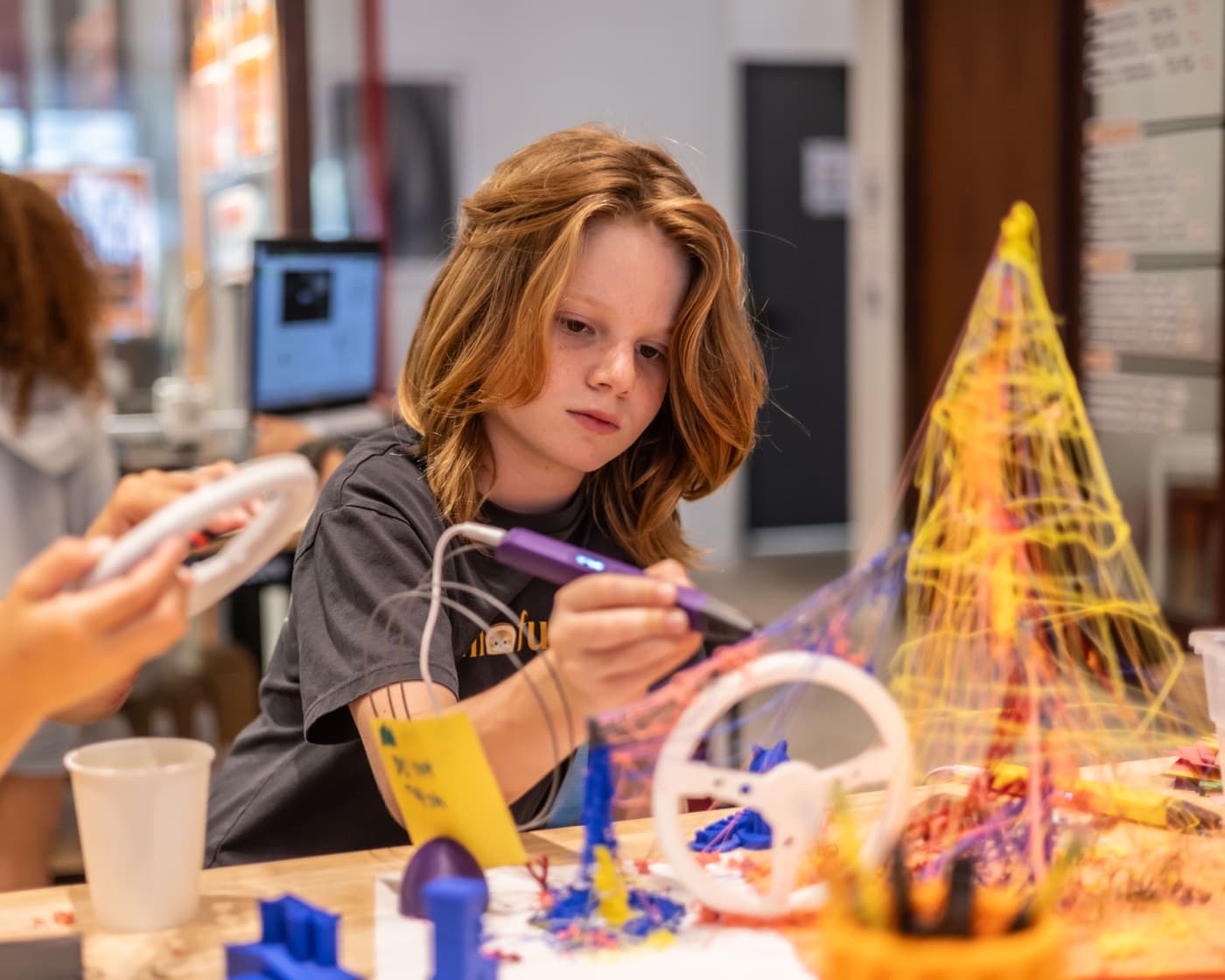 A kid grinning next to a glowing project they built at Forge.
