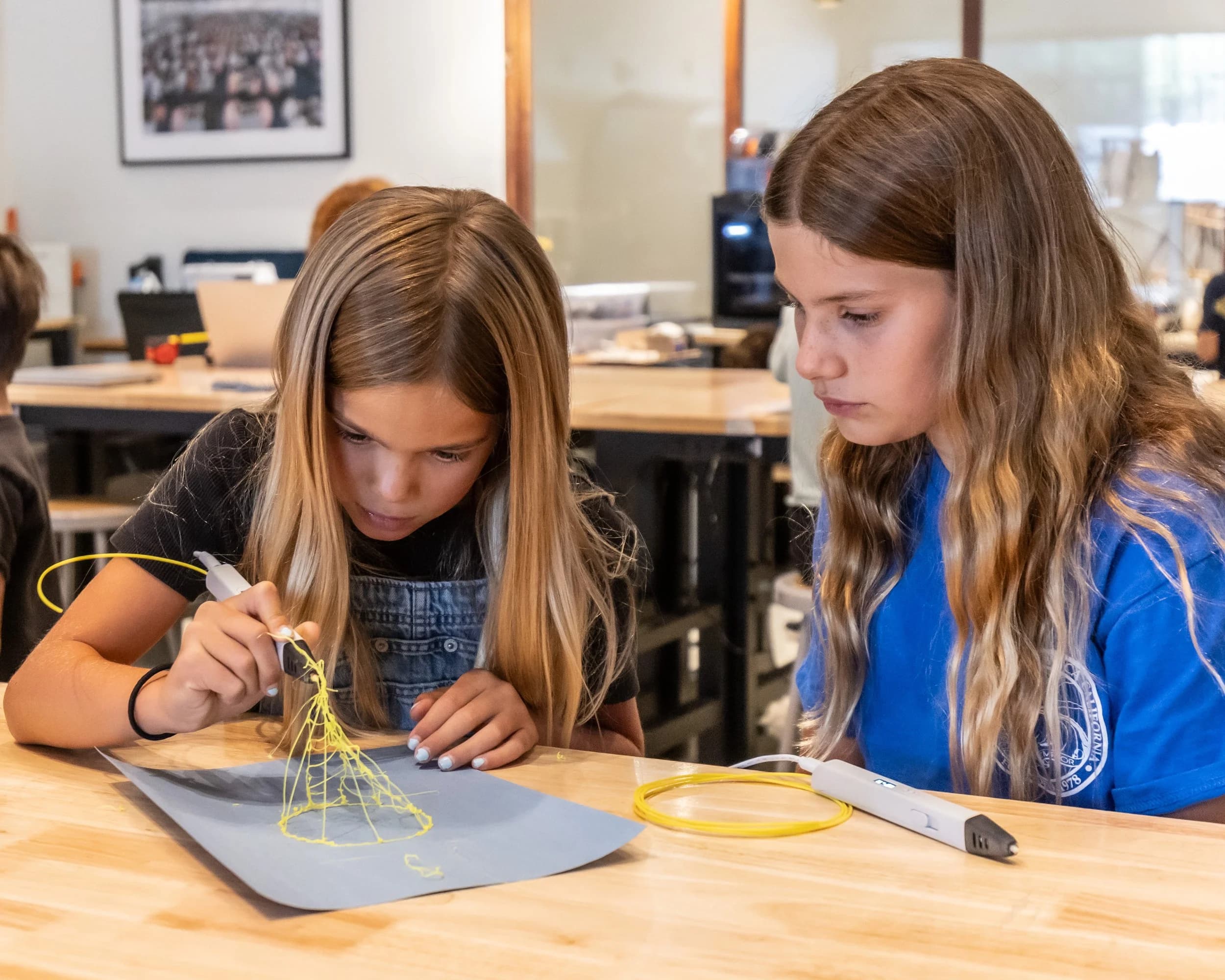 Two girls using 3D pens to build a project together at a Forge workbench.