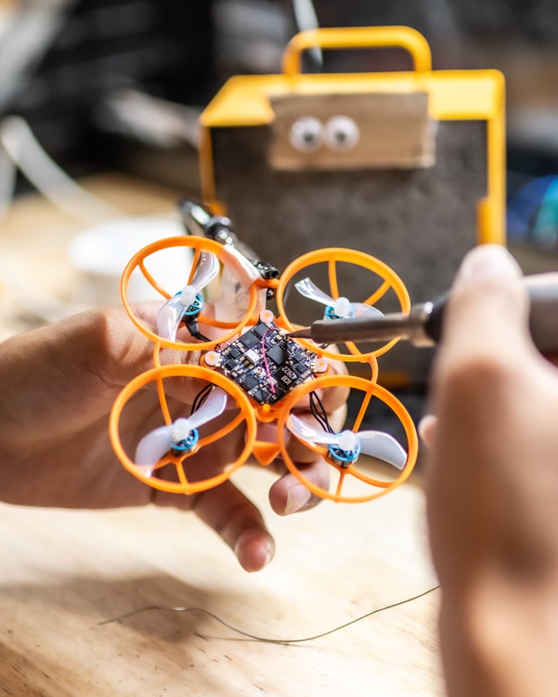 A camper's hands soldering the orange racing drone they built at Forge summer camp.