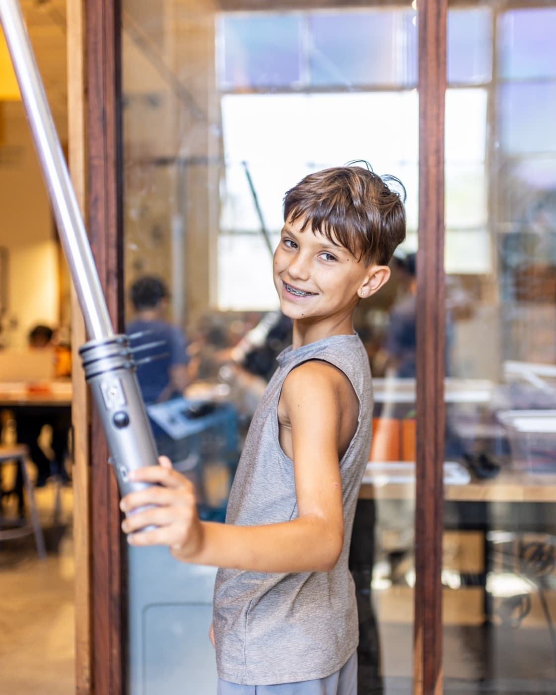 A smiling camper holding the full-size lightsaber he built at Forge summer camp.