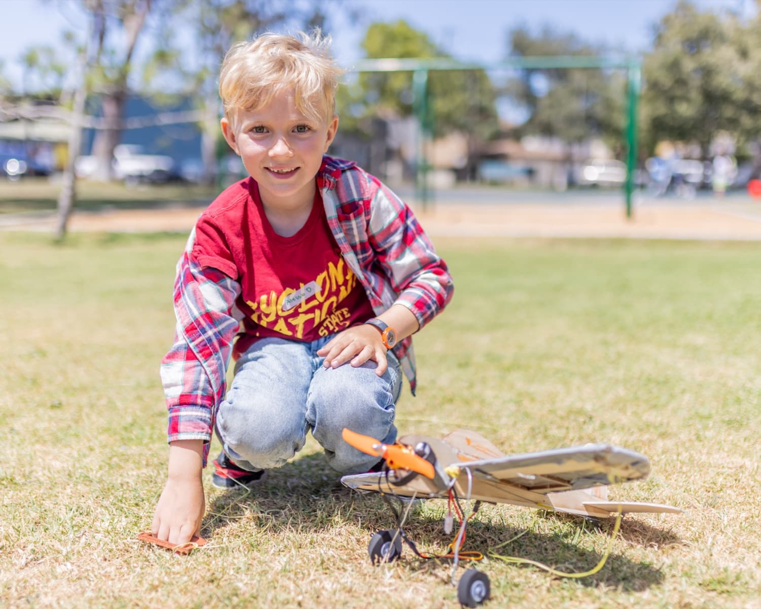 A camper crouched on the grass at Gandara Park with the model airplane he built at Forge summer camp.