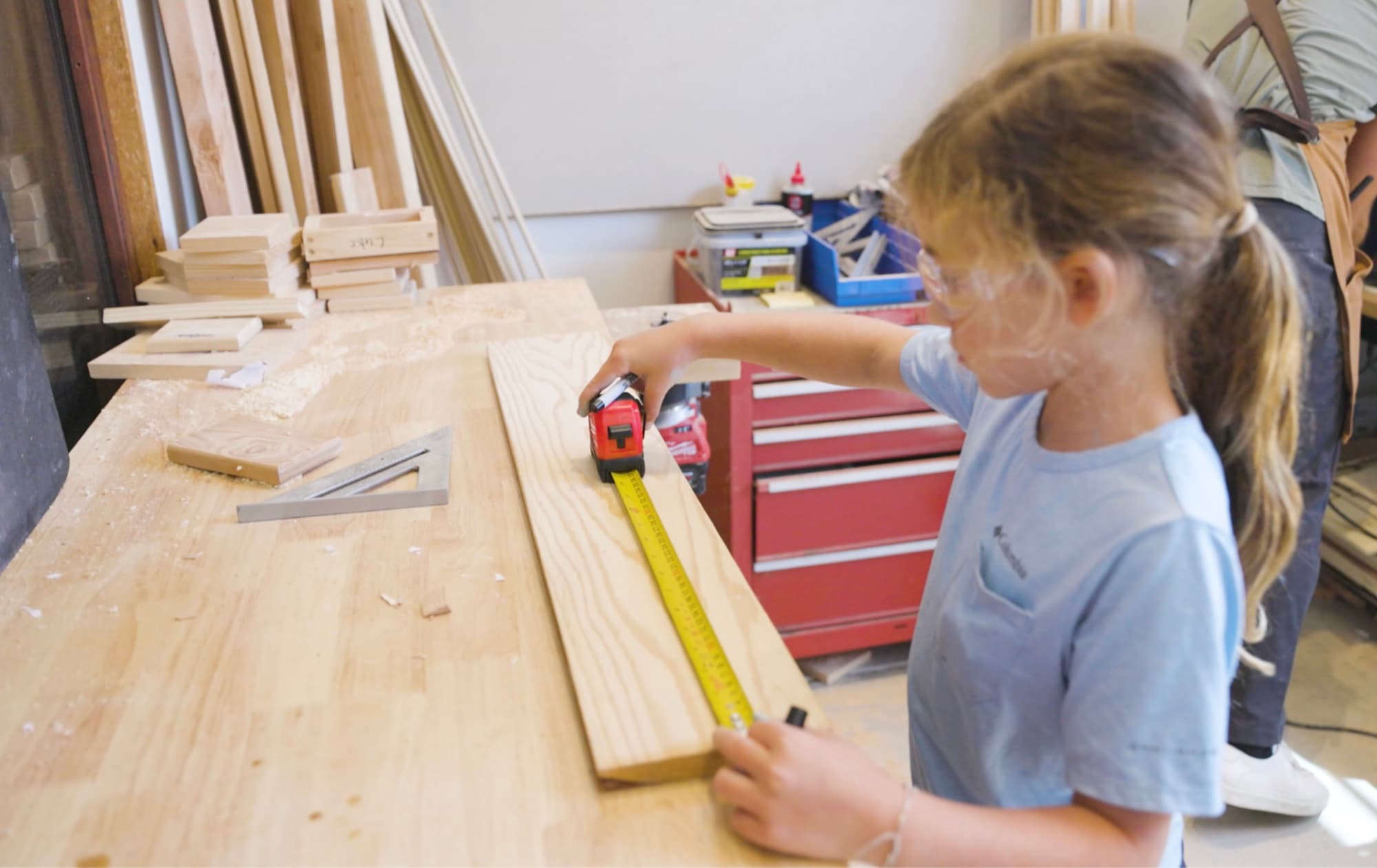 A young Forge student measuring a board with a tape measure.