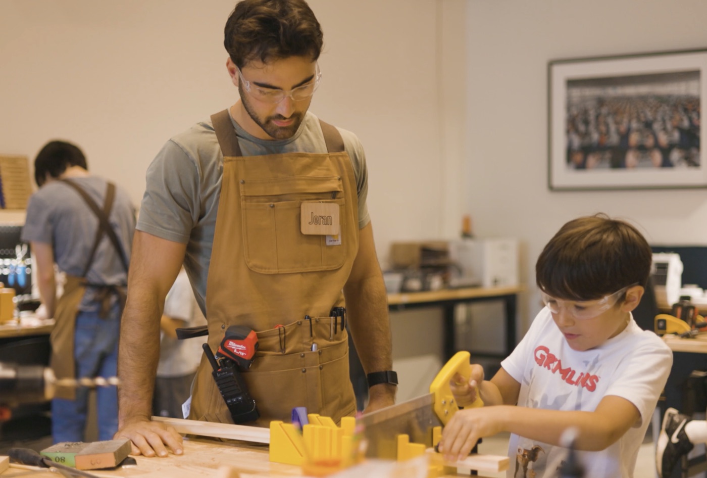 A Forge instructor guiding a young student sawing wood at the workshop bench.