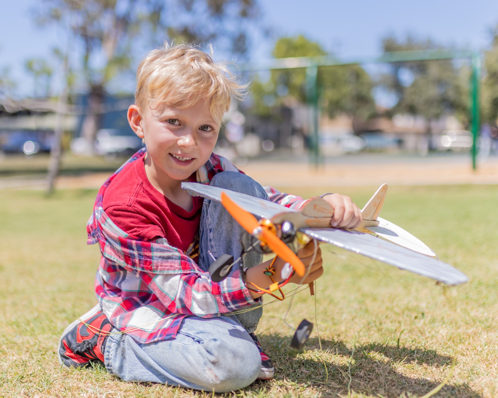 A camper kneeling on the grass at the park holding the model airplane he built and flew at Forge summer camp.